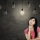 Thoughtful young businesswoman thinking idea while looking up with light bulbs